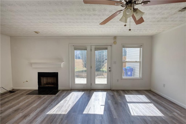unfurnished living room with a textured ceiling, wood finished floors, a wealth of natural light, and crown molding
