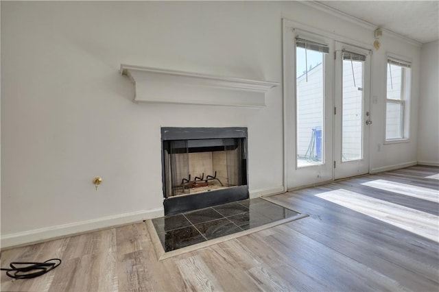 unfurnished living room featuring a fireplace with flush hearth, a healthy amount of sunlight, baseboards, and wood finished floors