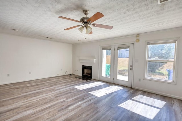 unfurnished living room featuring a fireplace with flush hearth, baseboards, light wood-style flooring, and a textured ceiling