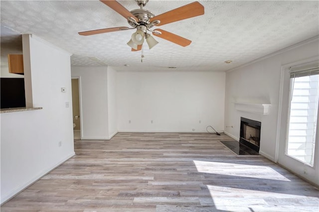 unfurnished living room featuring a textured ceiling, ceiling fan, light wood-style flooring, a fireplace with flush hearth, and baseboards