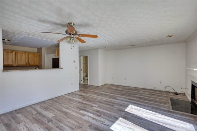 unfurnished living room featuring a textured ceiling, ceiling fan, a fireplace with flush hearth, and light wood-style flooring
