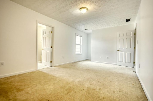 empty room featuring light carpet, visible vents, baseboards, and a textured ceiling