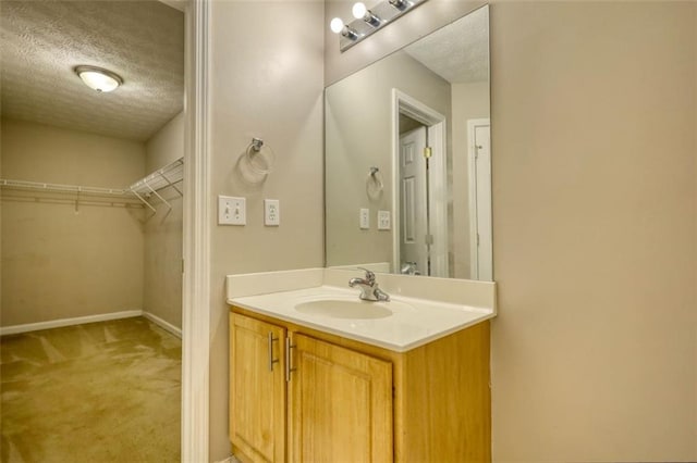 bathroom featuring baseboards, a textured ceiling, vanity, and a spacious closet