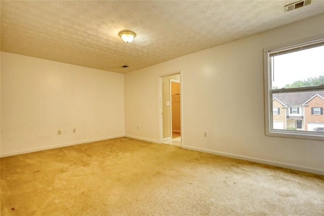 empty room featuring baseboards, light colored carpet, visible vents, and a textured ceiling