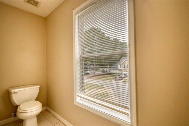 half bathroom with toilet, tile patterned flooring, visible vents, and baseboards