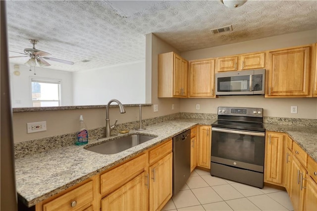 kitchen featuring visible vents, light stone countertops, stainless steel appliances, light brown cabinets, and a sink
