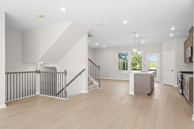 kitchen featuring appliances with stainless steel finishes, light hardwood / wood-style floors, sink, hanging light fixtures, and a kitchen island with sink