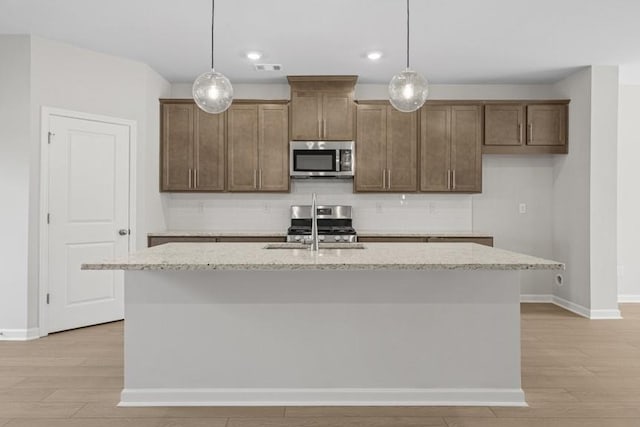 kitchen with light stone countertops, sink, stainless steel appliances, and a center island with sink