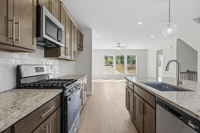 kitchen with light stone countertops, stainless steel appliances, sink, hanging light fixtures, and ceiling fan