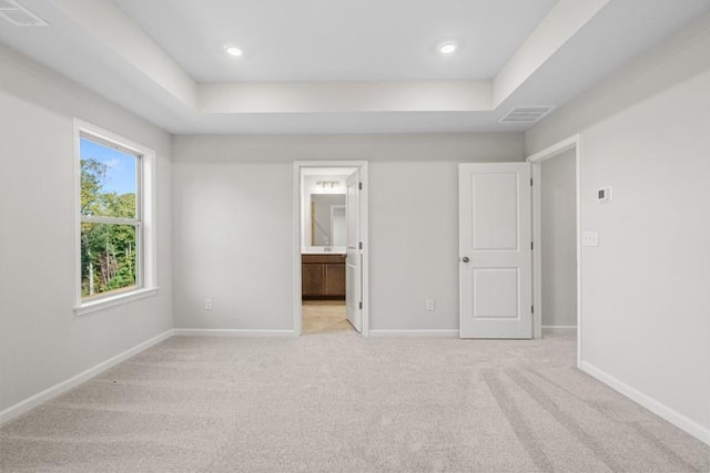 unfurnished bedroom with light colored carpet, a raised ceiling, and ensuite bath