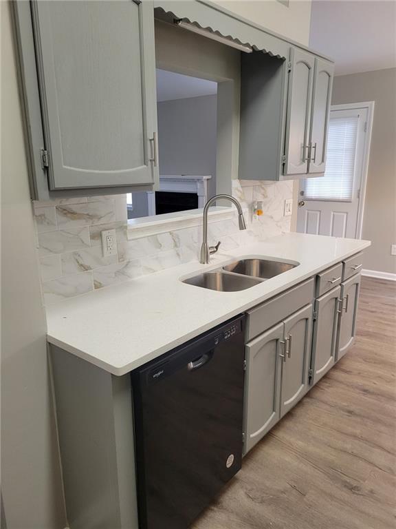 kitchen with dishwasher, light countertops, gray cabinetry, light wood-style floors, and a sink