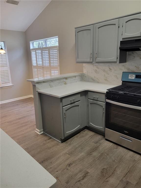 kitchen with stainless steel range with gas cooktop, gray cabinets, light countertops, a peninsula, and wall chimney exhaust hood