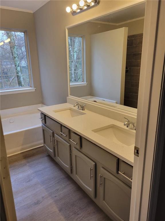 full bath featuring double vanity, a sink, a bath, and wood finished floors