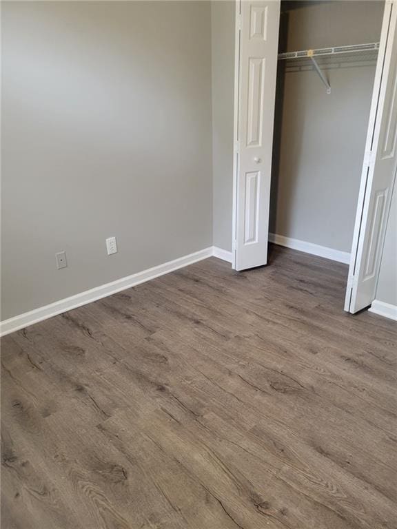 unfurnished bedroom featuring dark wood-type flooring, a closet, and baseboards