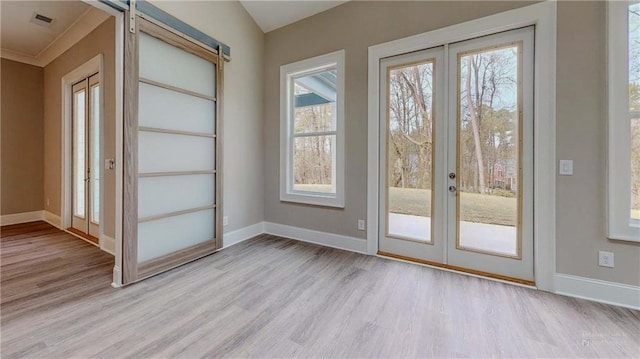 doorway with crown molding, light hardwood / wood-style floors, french doors, and a barn door