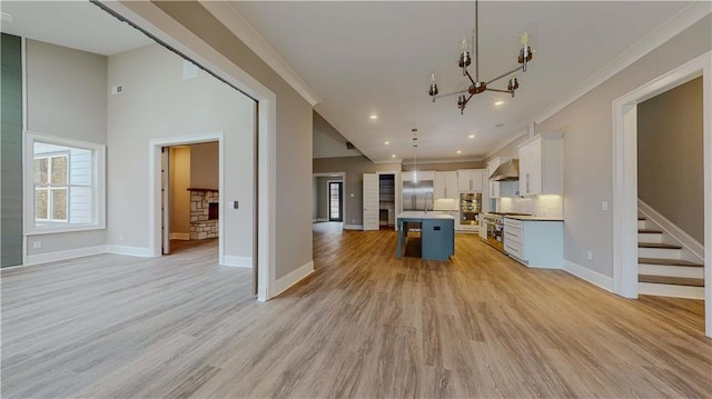 kitchen with a kitchen island with sink, light wood-type flooring, hanging light fixtures, high quality appliances, and white cabinets