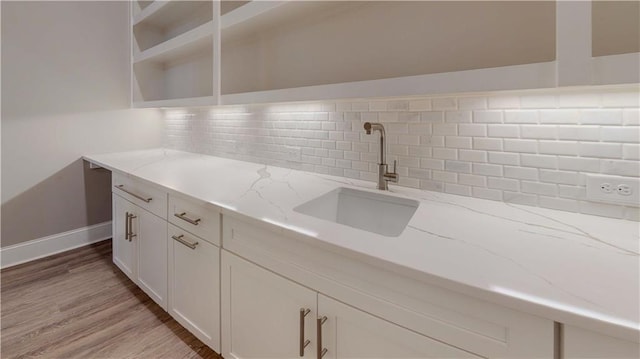 kitchen featuring white cabinets, tasteful backsplash, sink, light wood-type flooring, and light stone counters