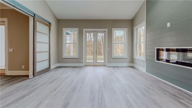 unfurnished living room with vaulted ceiling, a barn door, and light hardwood / wood-style flooring