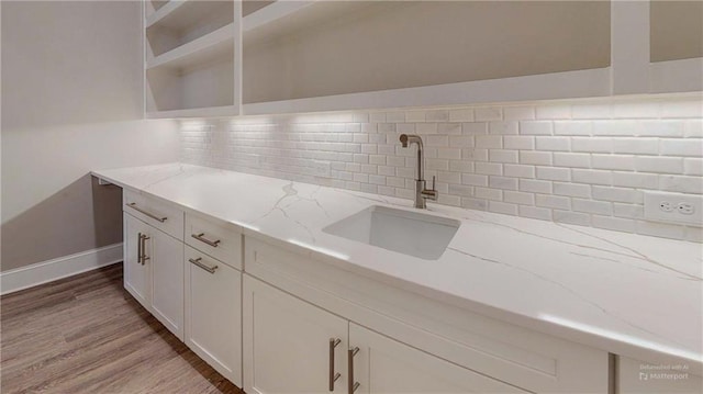 kitchen with light stone countertops, white cabinetry, sink, backsplash, and light wood-type flooring