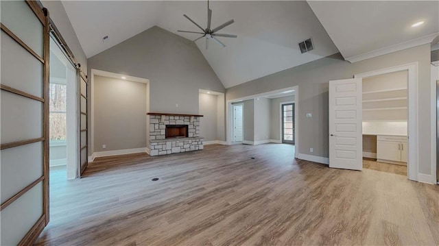 unfurnished living room featuring a barn door, ceiling fan, light wood-type flooring, a fireplace, and high vaulted ceiling