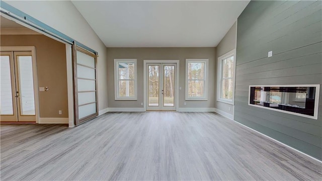 unfurnished living room featuring a barn door, vaulted ceiling, french doors, and light hardwood / wood-style flooring