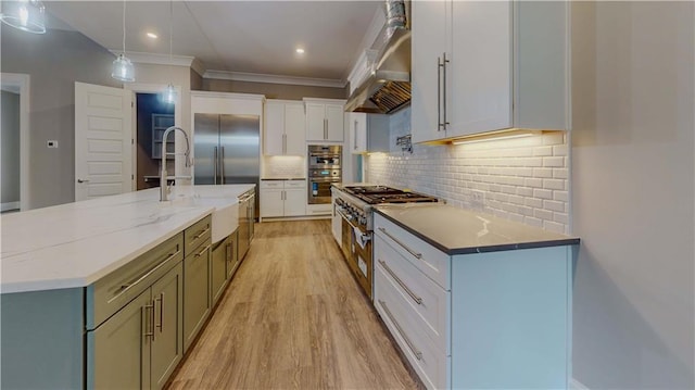 kitchen featuring white cabinetry, backsplash, decorative light fixtures, wall chimney exhaust hood, and a large island with sink