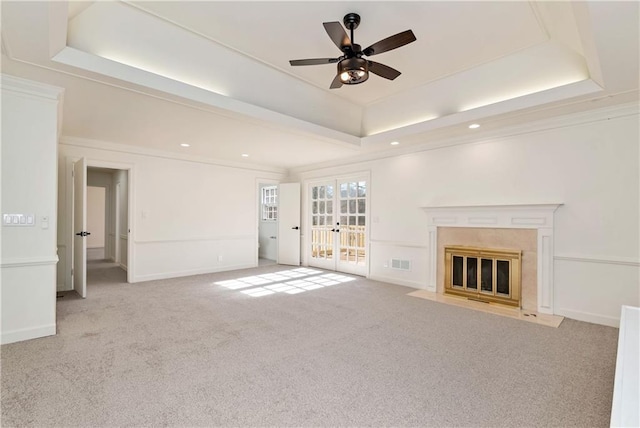 unfurnished living room with a tray ceiling, ceiling fan, a high end fireplace, light carpet, and french doors