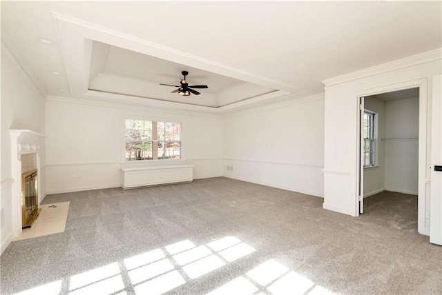 unfurnished living room with ceiling fan, light colored carpet, ornamental molding, and a raised ceiling