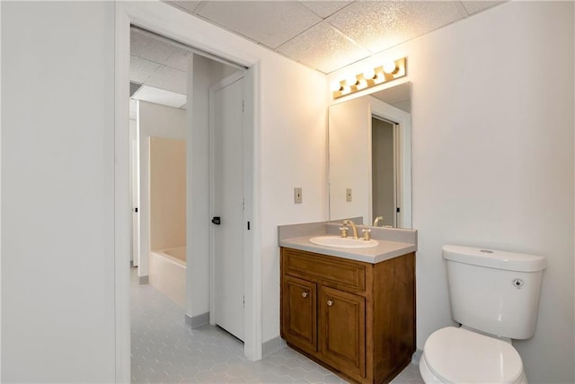 bathroom featuring a paneled ceiling, vanity, toilet, and a bathtub