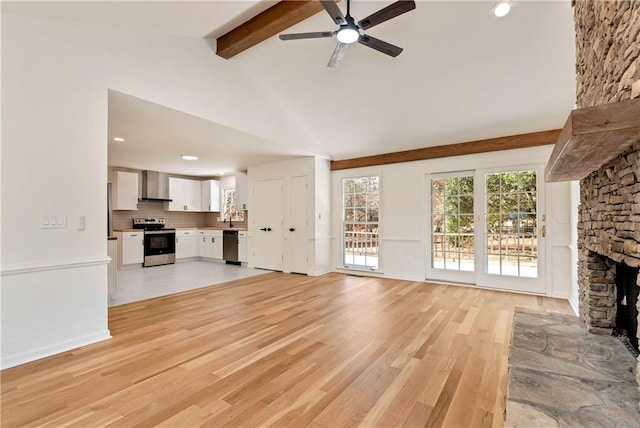 unfurnished living room featuring sink, ceiling fan, lofted ceiling with beams, a stone fireplace, and light wood-type flooring