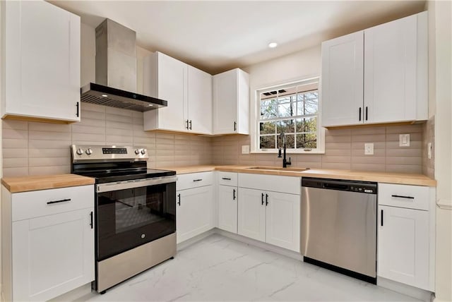 kitchen featuring white cabinetry, sink, butcher block counters, stainless steel appliances, and wall chimney exhaust hood