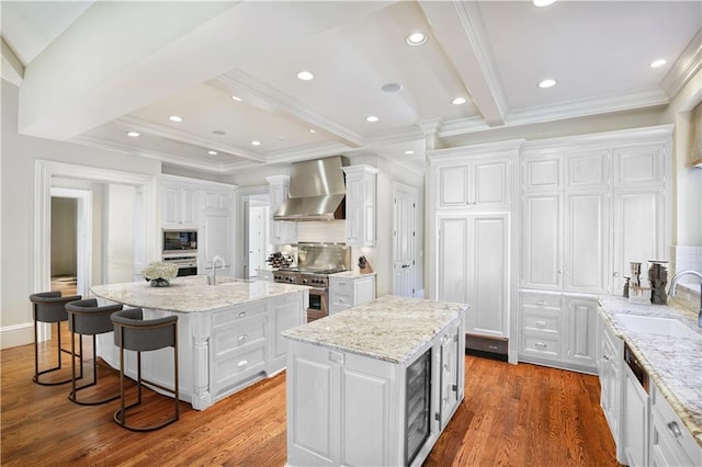 kitchen with white cabinetry, wall chimney exhaust hood, and an island with sink