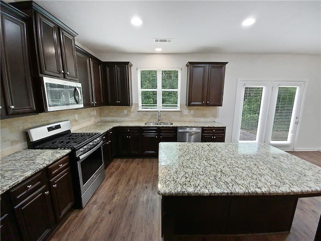 kitchen with stainless steel appliances, light stone counters, a center island, sink, and dark wood-type flooring