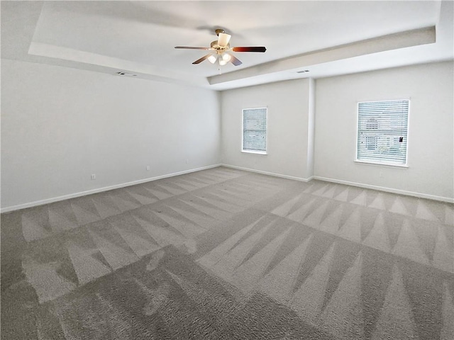 unfurnished room with carpet floors, a raised ceiling, a ceiling fan, and baseboards