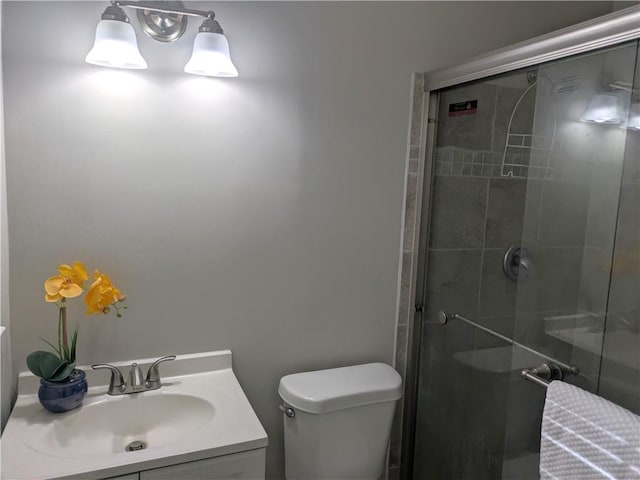 bathroom with a shower with shower door, vanity, and toilet