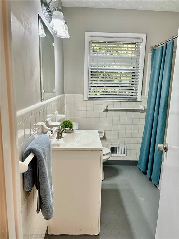 bathroom featuring tile patterned floors, vanity, toilet, and tile walls