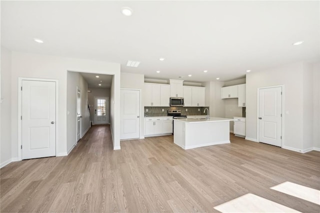 kitchen with white cabinets, a kitchen island with sink, light wood-type flooring, stainless steel appliances, and sink