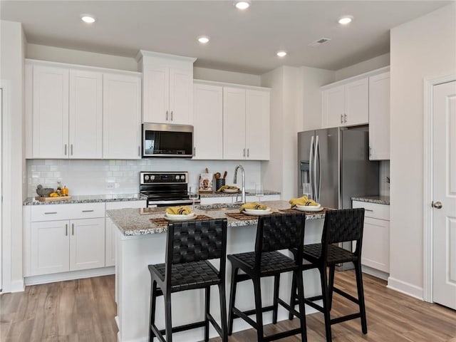 kitchen featuring sink, stainless steel appliances, white cabinets, light stone counters, and a center island with sink