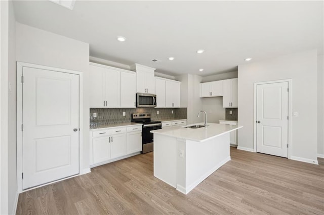 kitchen with light hardwood / wood-style floors, white cabinets, stainless steel appliances, and an island with sink