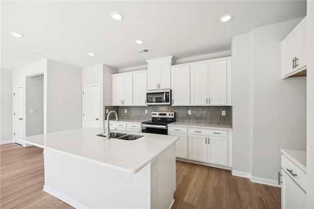 kitchen with appliances with stainless steel finishes, white cabinets, sink, and an island with sink