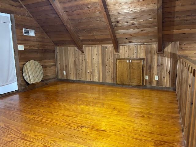 additional living space with wood walls, wood-type flooring, lofted ceiling with beams, and wooden ceiling