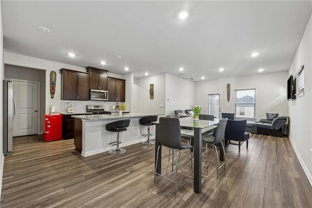 kitchen featuring dark wood-type flooring, a breakfast bar area, stainless steel appliances, light stone countertops, and an island with sink