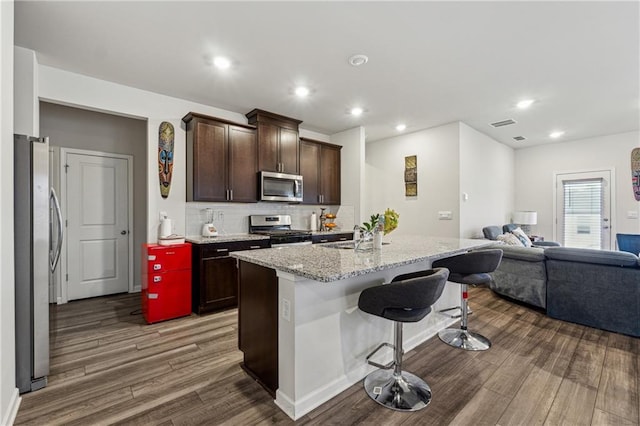 kitchen featuring a kitchen island with sink, light stone counters, dark hardwood / wood-style flooring, and appliances with stainless steel finishes