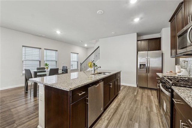 kitchen featuring sink, a kitchen island with sink, stainless steel appliances, light hardwood / wood-style floors, and light stone countertops