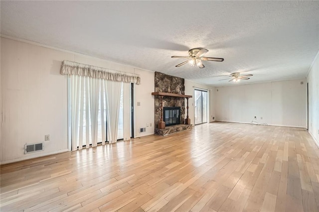 unfurnished living room with ceiling fan, a stone fireplace, a textured ceiling, and light hardwood / wood-style floors