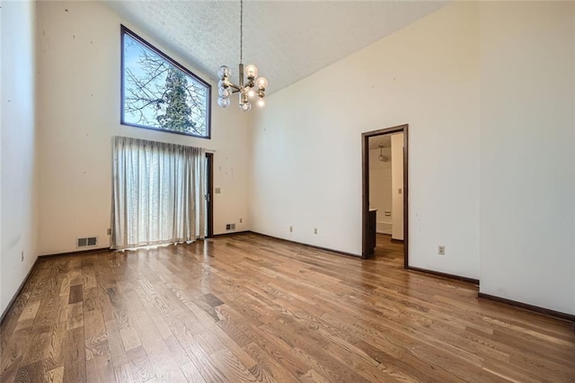 unfurnished dining area featuring a notable chandelier, wood-type flooring, high vaulted ceiling, and a textured ceiling