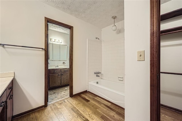 bathroom with tiled shower / bath combo, wood-type flooring, vanity, and a textured ceiling