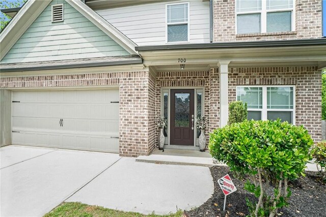 view of exterior entry featuring brick siding, concrete driveway, and an attached garage