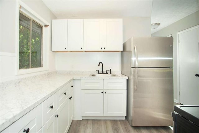 kitchen with light stone counters, freestanding refrigerator, a sink, white cabinetry, and light wood-type flooring