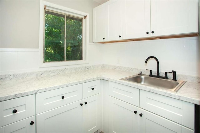 kitchen featuring light stone countertops, white cabinetry, and a sink